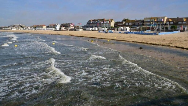 Een strand met golven, gebouwen en een heldere lucht.