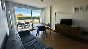 Een woonkamer met een bank, een televisie, een eettafel met stoelen en een balkon met uitzicht.