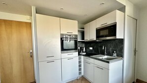Een kleine keuken met witte kastjes, een inbouwoven, een magnetron en een spoelbak.