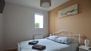 Een slaapkamer met een bed, een raam, een schilderij en een nachtkastje.