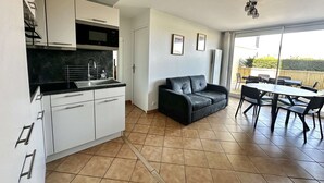Een moderne keuken met witte kastjes en een zwart aanrecht, een zwarte leren bank en een eethoek met een tafel en stoelen.