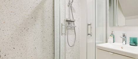 Un baño moderno con ducha de vidrio, un lavamanos blanco con espejo arriba y un mueble blanco debajo.