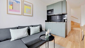 Un salon moderne avec un canapé gris, une petite table noire surmontée d’un vase, et un coin cuisine doté de meubles gris et d’un four à micro-ondes.