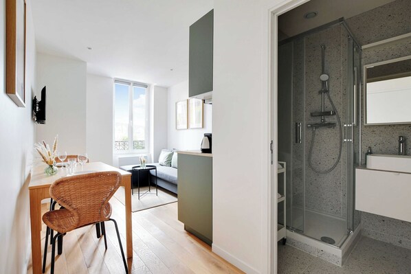 A modern apartment with a dining area, a sofa, and a glass-enclosed shower.
