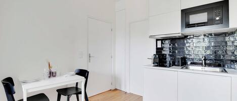 A modern kitchen with white cabinetry, a black microwave, and a tiled backsplash.