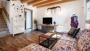 Uma sala de estar com teto de madeira, uma TV, um sofá, uma mesa de centro e uma escada.