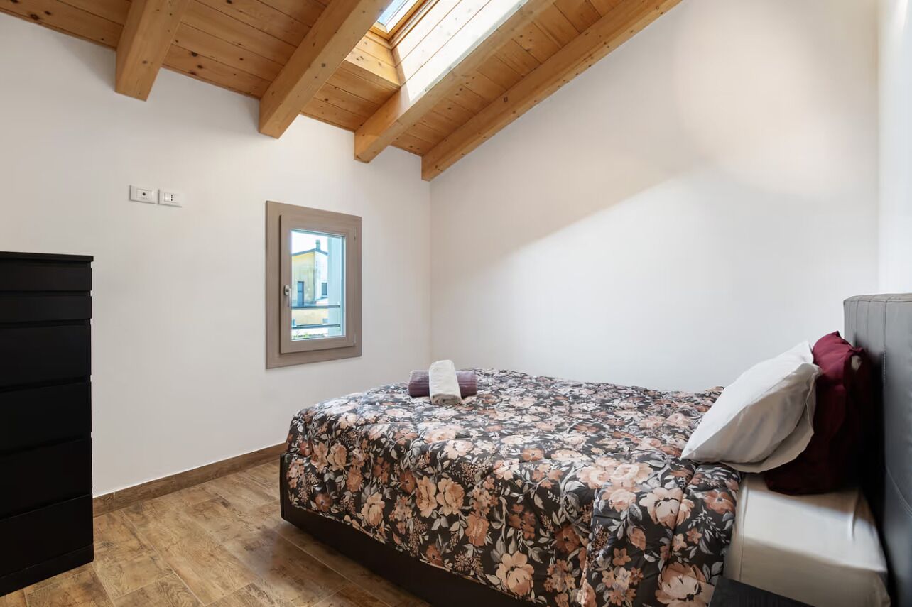 Quarto com teto de madeira, cama com colcha florida, janela e porta.