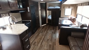 Un intérieur de camping-car compact comprenant un coin cuisine, un espace repas et un coin nuit.