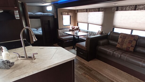 Un intérieur de camping-car compact comprenant un coin cuisine, un espace salon avec un canapé et une table, ainsi qu’une fenêtre laissant entrer la lumière naturelle.