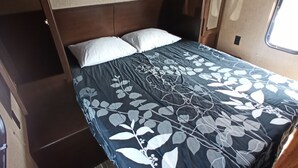 Un lit avec une couvre-lit à motifs floraux, une tête de lit en bois et une fenêtre avec des stores.