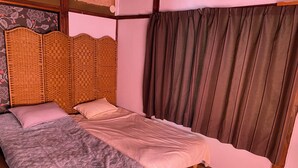Un lit simple avec une tête de lit en bois, une couvre-lit matelassée grise et un rideau marron.