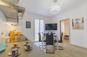 Una cocina moderna con comedor, un televisor montado en la pared y una escalera que sube a otro nivel.