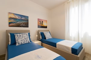 Habitación de hotel con dos camas, cada una con cubrecama y almohadas azules a juego. Hay dos cuadros colgados en la pared que representan una playa y un atardecer.