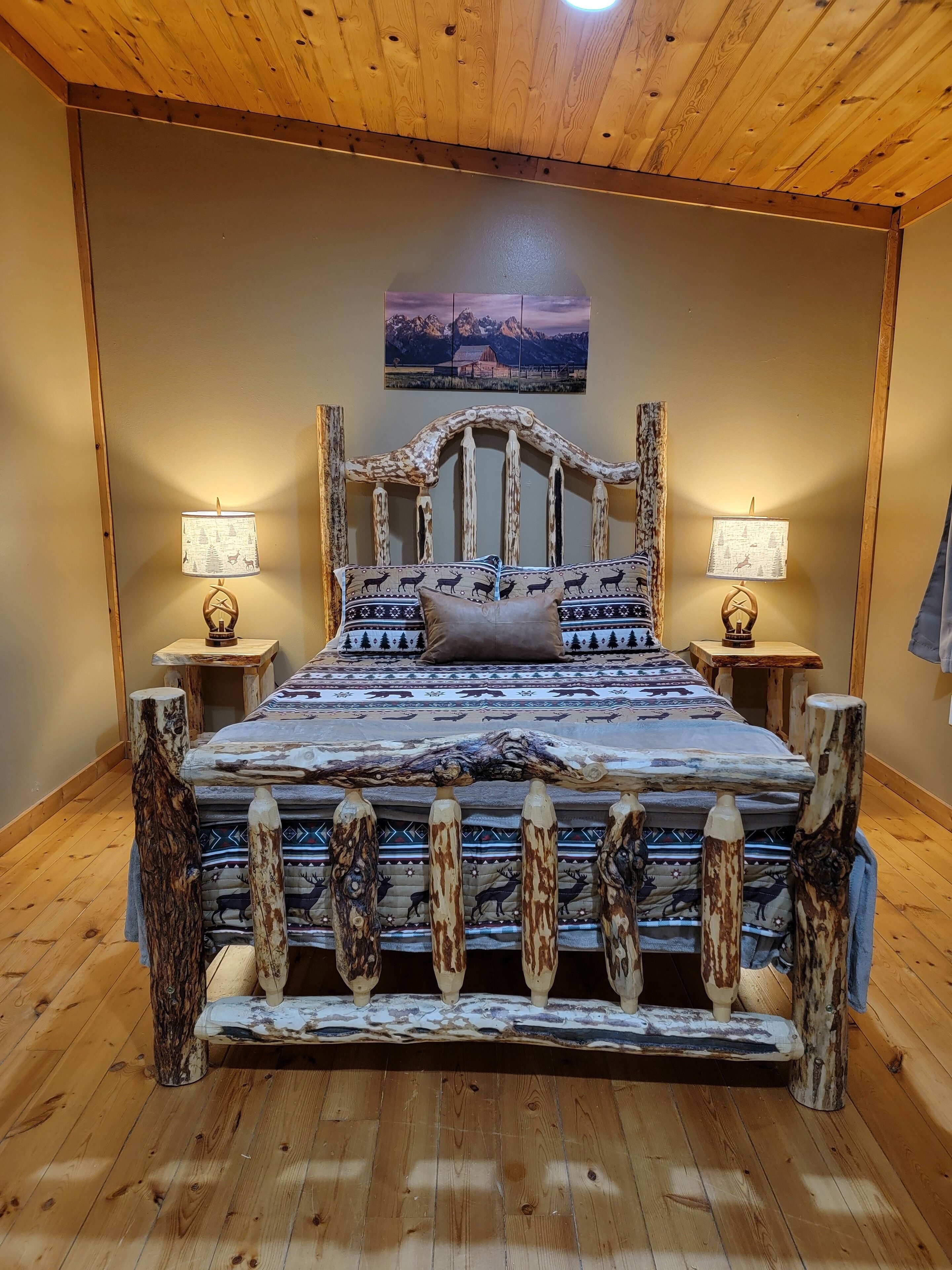 A wooden-framed bed with a patterned bedspread, two bedside lamps, and a painting on the wall.