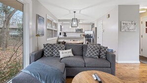 A modern living room with a gray sectional sofa, a wooden coffee table, and a kitchen in the background.