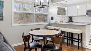 A modern kitchen with white cabinets, a central island with bar stools, and a dining area with a round table and chairs.