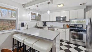 A modern kitchen with white cabinetry, stainless steel appliances, a large island with bar stools, and a checkered floor.