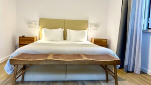 A neatly made bed with a headboard, two bedside tables, and a woven bench at the foot of the bed. - Villa Inn Sintra | Private Garden Retreat (Sintra)