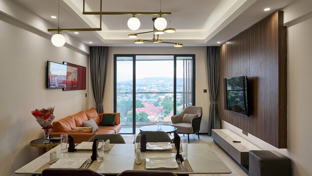 Un salon moderne comprenant un coin repas, de grandes fenêtres, un téléviseur à écran plat et une vue sur la ville.