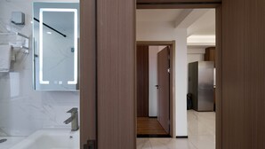 Une salle de bain moderne avec un lavabo en marbre, un miroir doté d’un éclairage intégré et une porte en bois donnant sur un couloir.