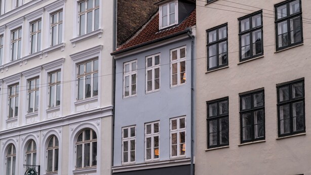 Una hilera de edificios de varios pisos con fachadas blancas y grises, que presentan ventanas en arco y una variedad de estilos de ventanas.