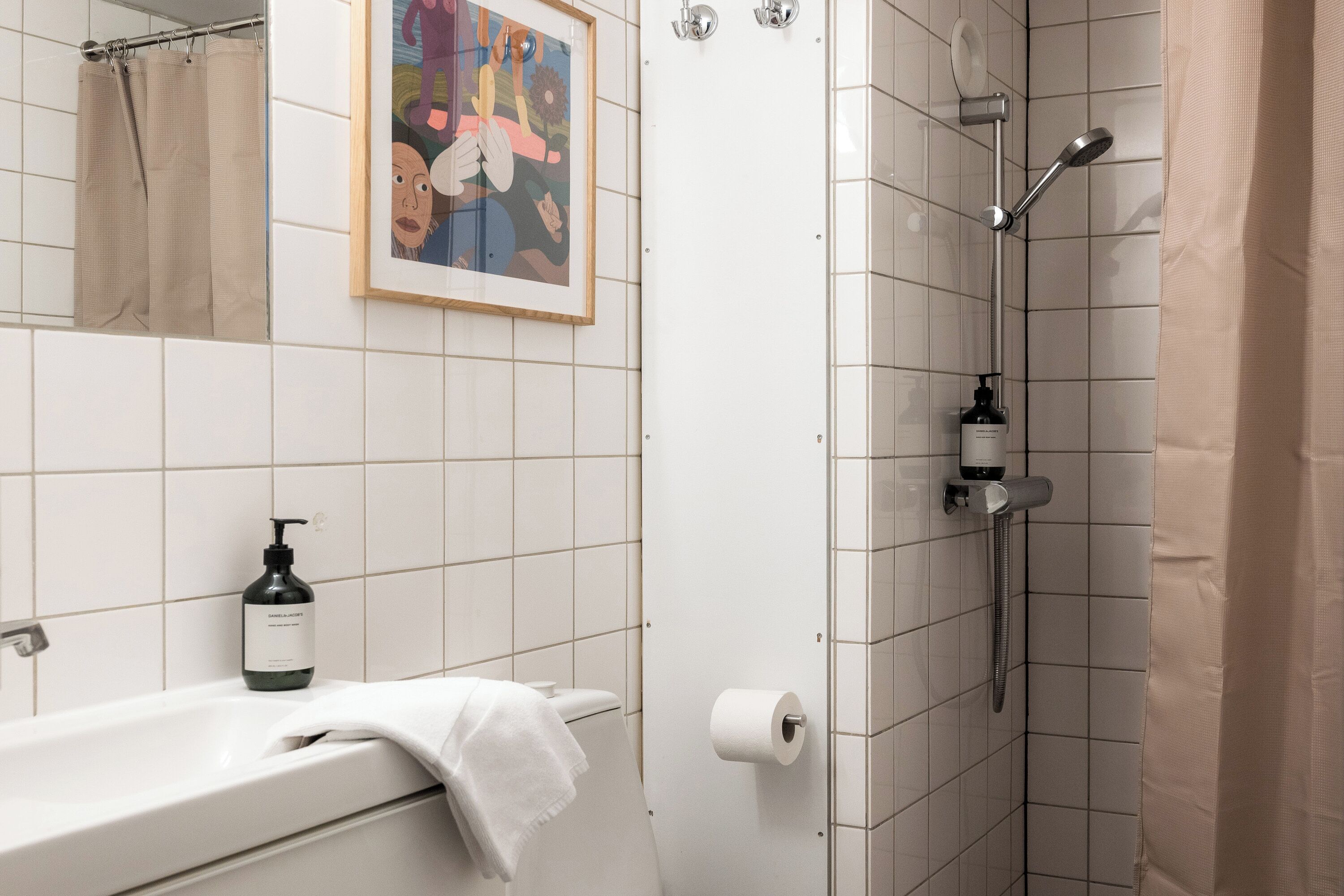 A bathroom with a bathtub, a shower, a toilet, a framed picture on the wall, and a bottle of hand soap.