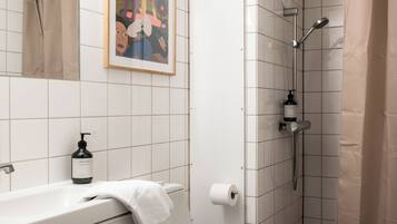 A bathroom with a bathtub, a shower, a toilet, a framed picture on the wall, and a bottle of hand soap.