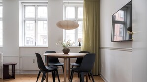 Un comedor con una mesa redonda, cuatro sillas, un florero con flores y una lámpara colgante.