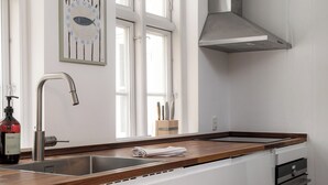 Una cocina con un lavamanos de acero inoxidable, armarios blancos, un piso a cuadros blanco y negro, y una ventana con vistas al exterior.