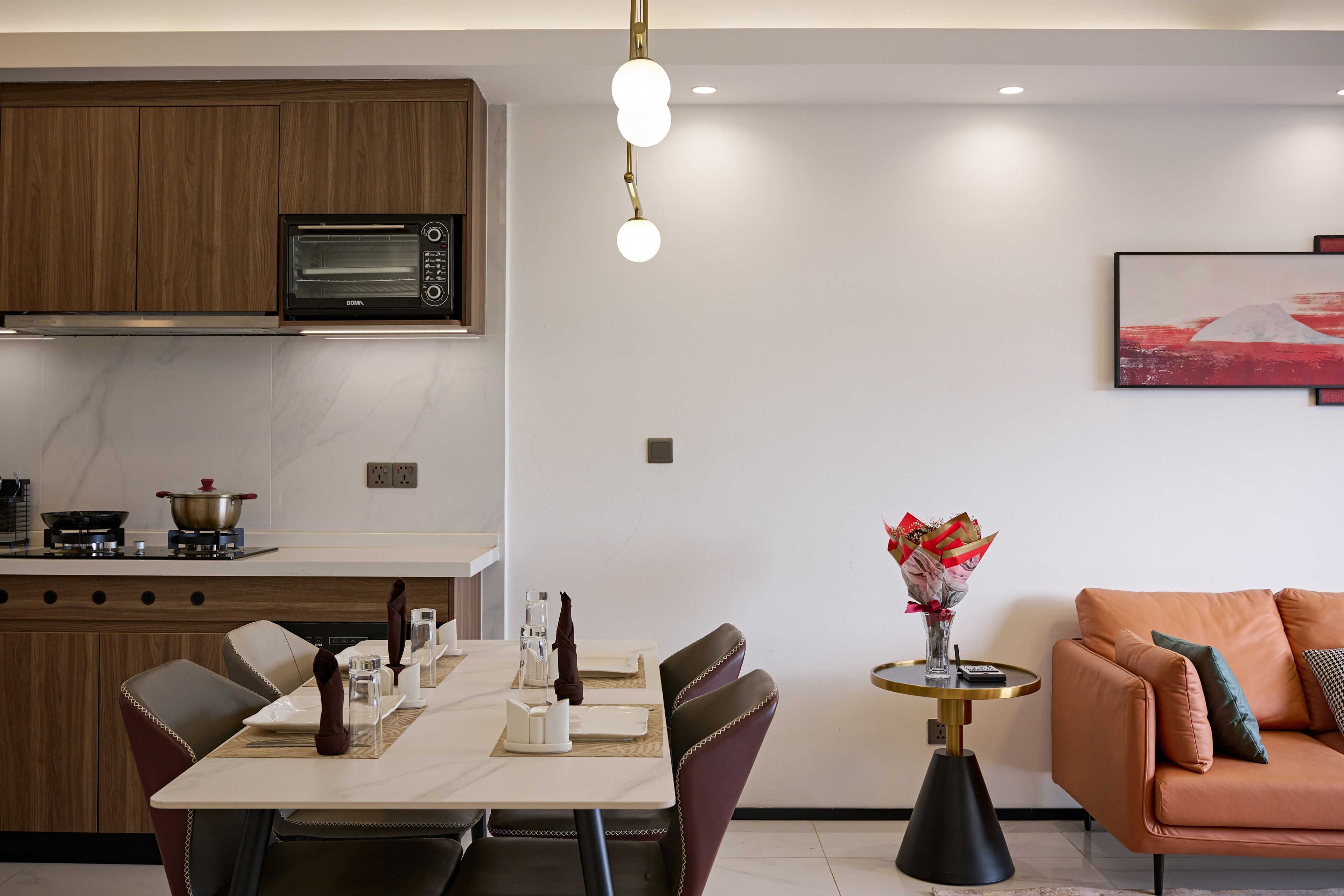 A modern kitchen with a built-in microwave, a dining table set for four, and a sofa in the living area.
