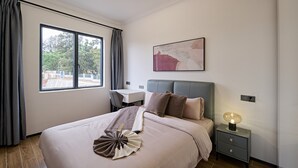 A modern hotel room with a large bed, a desk, and a view of the outdoors. - 3-Bedroom apartment at Oasis Park. (Kigali)