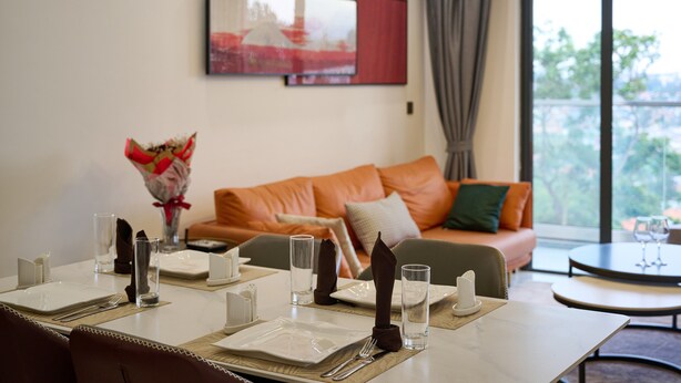 A dining area with a table set for four, a sofa in the background, and a window with a view of greenery.