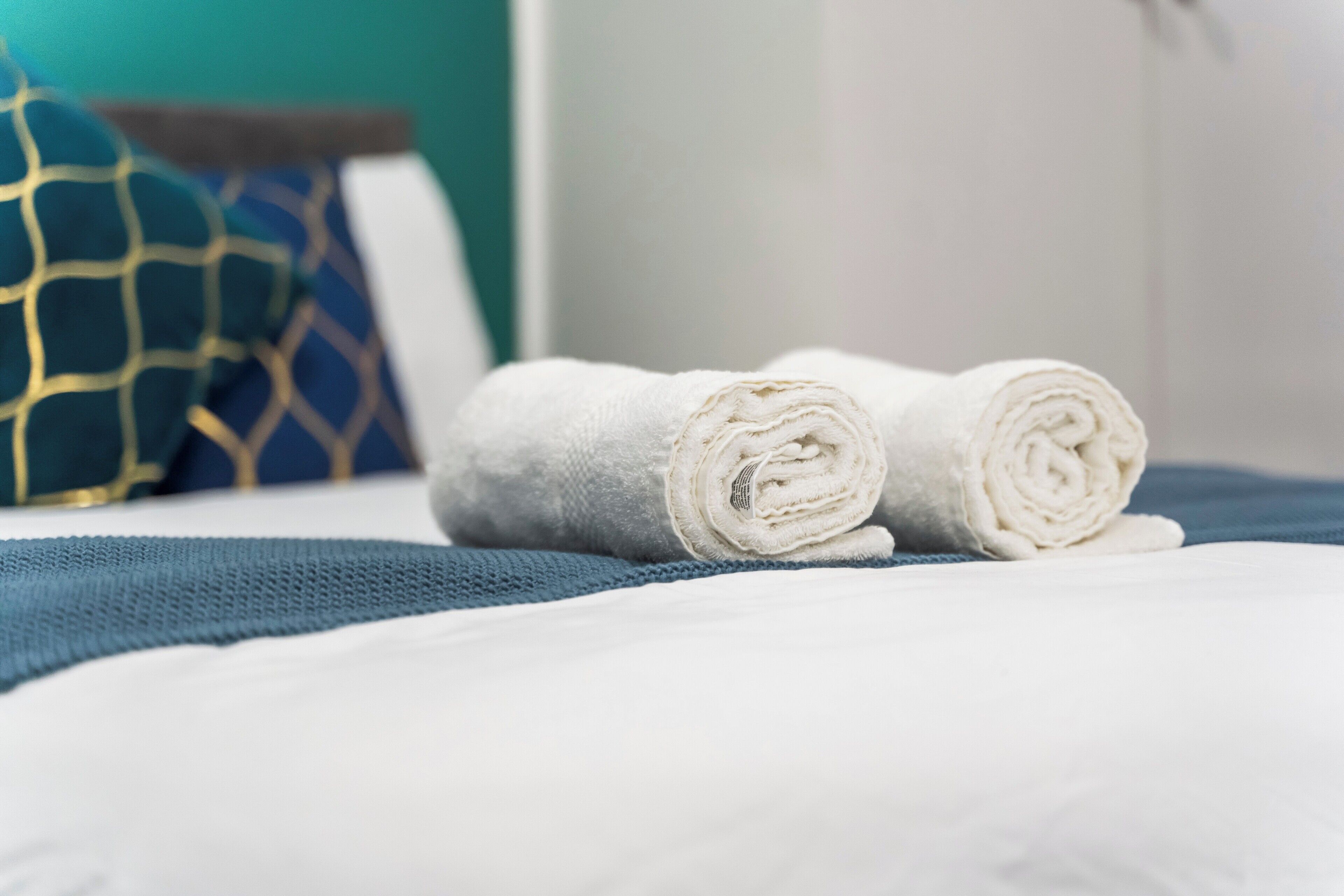A neatly made bed with white linens and a blue blanket.