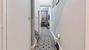 Un pasillo estrecho con alfombra estampada, una puerta a la izquierda y un televisor fijado a la pared a la derecha.