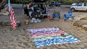 Un terrain de camping avec un véhicule, des chaises de camping et une couverture sur le sable.