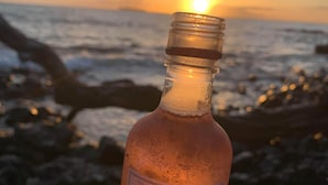 A hand holding a bottle of Sutter Home wine with a sunset and ocean in the background. - Easy Campers Maui - Paradise Jays Maui Island Breeze (Kihei)