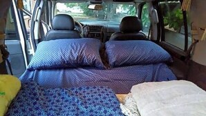 A compact vehicle interior with a bed, a small table, and a window. - Easy Campers Maui - Paradise Jays Maui Island Breeze (Kihei)