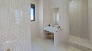 A bathroom with a white tiled wall, a window, a sink with a mirror, and a shelf with toiletries. - Spectacular apartment in Cuatro Caminos (Madrid)