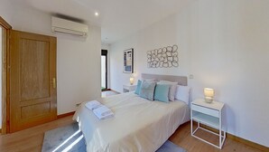 A bedroom with a bed, bedside tables, a wall-mounted air conditioner, and a wooden door. - Spectacular apartment in Cuatro Caminos (Madrid)