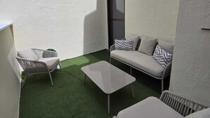 A small, enclosed outdoor space with artificial green turf, two wicker chairs, a white sofa with patterned cushions, and a small table. - Spectacular apartment in Cuatro Caminos (Madrid)