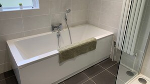 Een moderne badkamer met een witte badkuip, een douchecabine met glazen wanden en een raam met kleine potplanten.