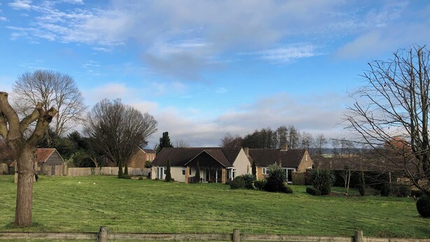 Een landelijke omgeving met huizen, een grasveld en een houten omheining.