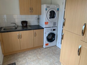 A compact kitchen with wooden cabinets, a sink, a coffee maker, and stacked washing machines.
