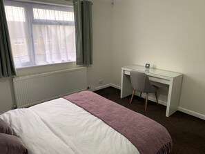 A bedroom with a bed, a desk, and a chair.