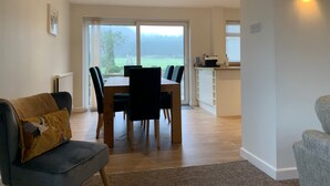 Een moderne woonkamer met een eetgedeelte, een keuken en uitzicht op een groen landschap.
