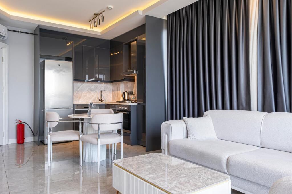 A modern living room with a white sofa, a marble coffee table, and a dining area with a white table and chairs.