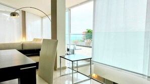 Un salon moderne avec un canapé, une table à manger et une chaise. Une grande fenêtre offre une vue sur l’extérieur.