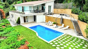 Une maison moderne à deux étages, dotée d’une piscine, d’un espace salon extérieur et d’un escalier menant à une terrasse en bois.