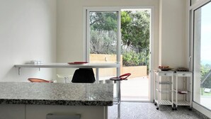 Une cuisine moderne avec un comptoir en granit, une chaise noire, une table blanche et une porte-fenêtre coulissante donnant sur un espace extérieur.