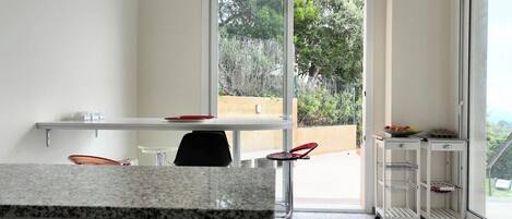 A modern kitchen with a granite countertop, a black chair, a white table, and a sliding glass door leading to an outdoor area.